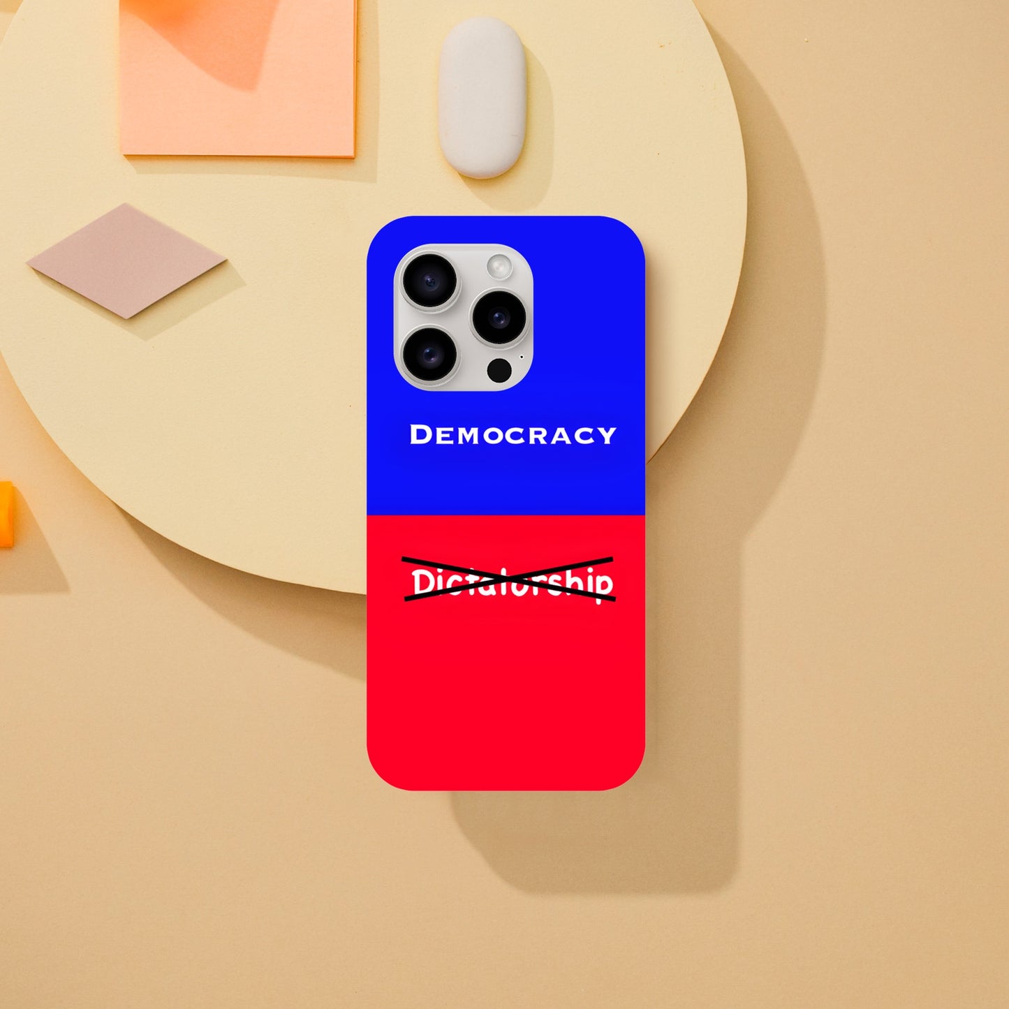 An Apple iPhone 15 Pro Phone Case with the following design on it: A visual comparison of two posters, the one on top features the term "Democracy”; written in white, against a royal blue background, and the one of the bottom features the term “Dictatorship" which is also written in white but is crossed out by two black lines, highlighting the preference for Democracy.